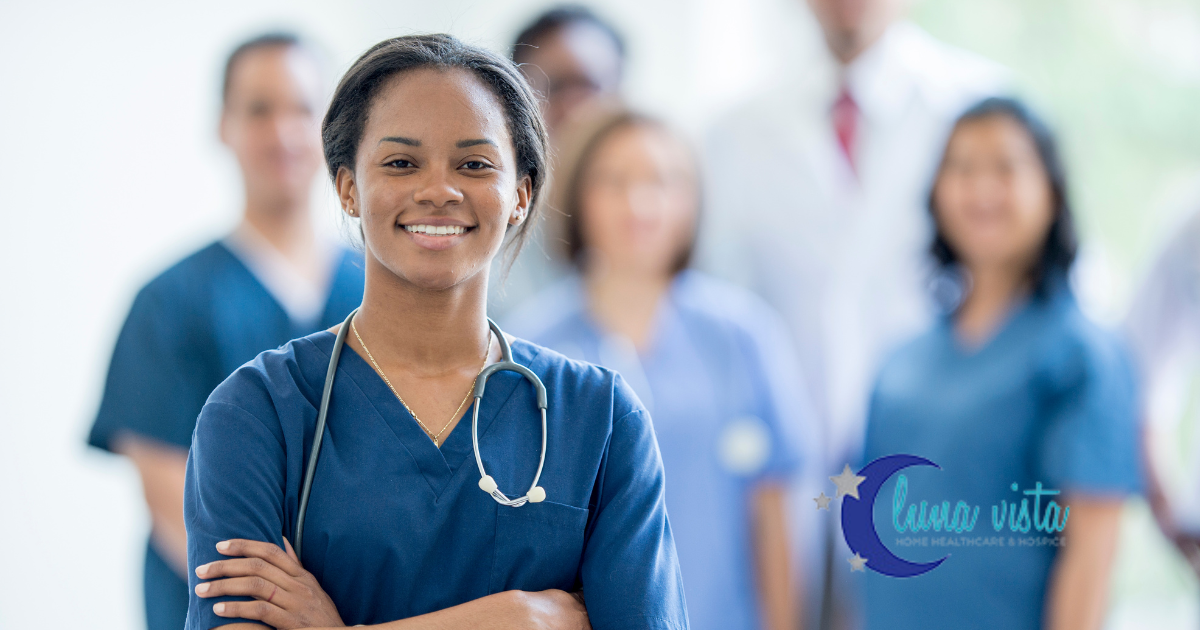 A smiling nurse stand with other nurses and professionals in the background.