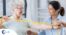 A woman helps an older woman exercise with a resistance band, showing how in-home physical therapy can help.